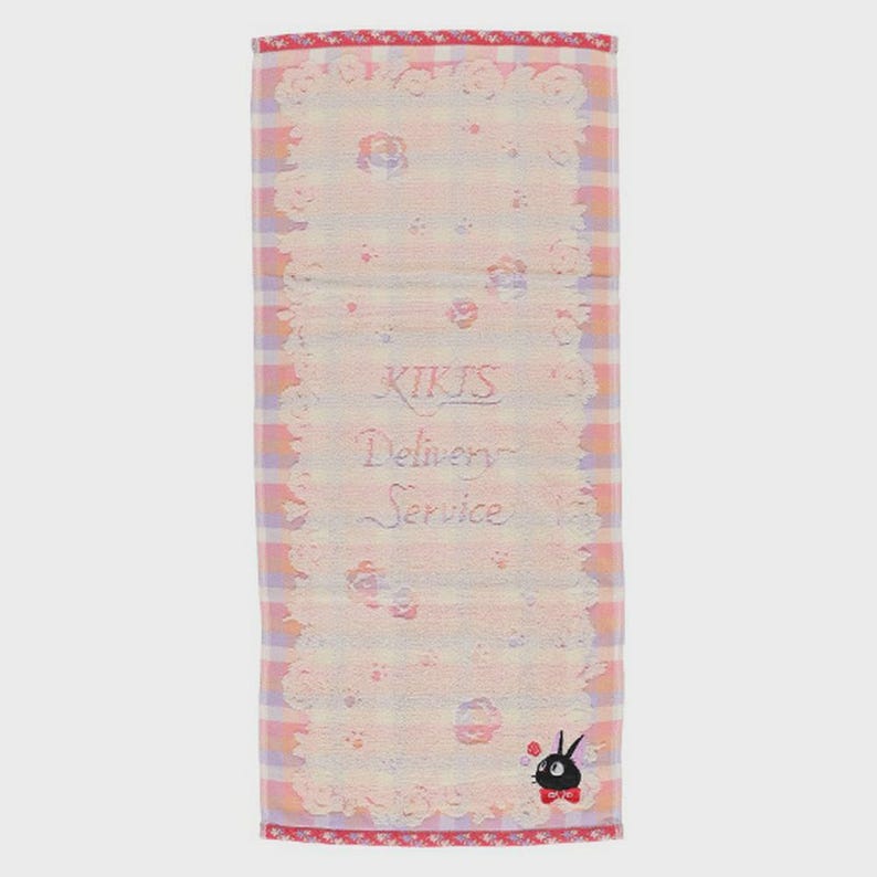May include: A rectangular, light pink and white checked towel with a floral lace border. The towel features the text "KIKI'S Delivery Service" in cursive script. A black cat with a red bow tie is at the bottom.