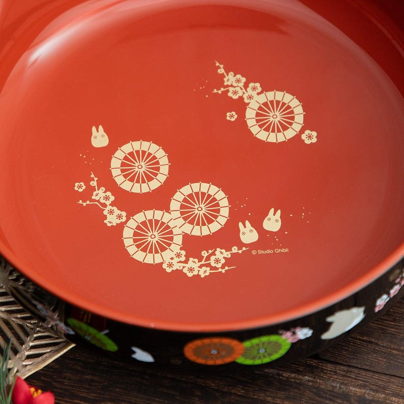 May include: A red serving tray with a black rim, featuring a decorative design of white umbrellas, flowers, and cartoon characters. The tray has a glossy finish and is suitable for serving food or displaying items.