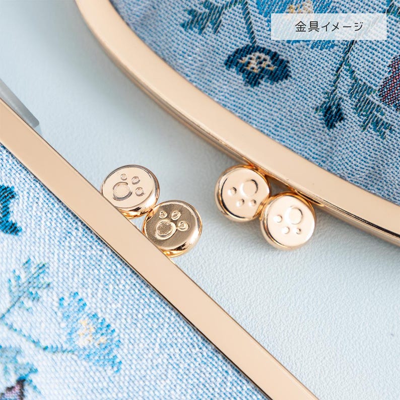 May include: Close-up of a light blue fabric purse with a floral pattern. The purse has a gold metal frame with three small gold metal paw print accents.