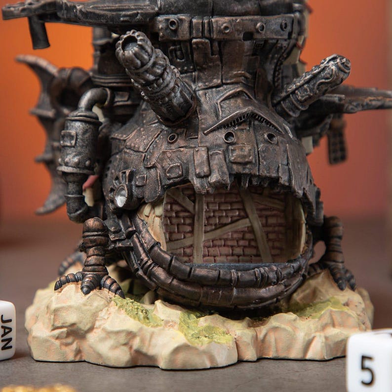 May include: A detailed, steampunk-style sculpture with a dark metallic finish. The sculpture features intricate mechanical details, a brick-lined opening, and is set on a textured base. The overall design suggests a fantasy or sci-fi theme.