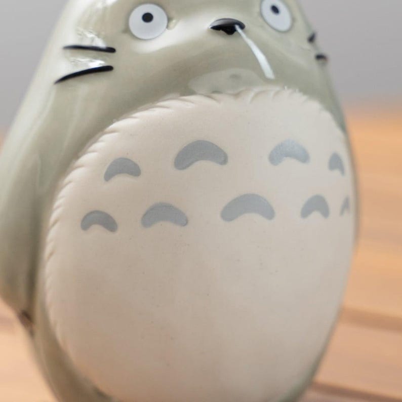 Puede incluir: Una figura de cer&aacute;mica de Totoro, un personaje de la pel&iacute;cula de animaci&oacute;n Mi vecino Totoro. La figura es de color gris claro con una barriga color crema y marcas grises en forma de media luna. Tiene ojos negros, nariz negra y una peque&ntilde;a gota blanca.