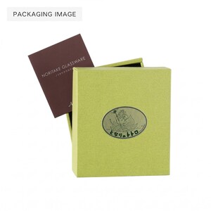May include: A light green box with a decorative oval emblem and Japanese text. A brown card with the text "NORITAKE GLASSWARE" is partially visible inside the box. The image is labeled "PACKAGING IMAGE".