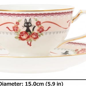 May include: A cream-colored teacup and saucer set with a black cat illustration and floral accents. The cup is 2.4 inches tall and the saucer is 5.9 inches in diameter. Gold trim edges the cup and saucer.