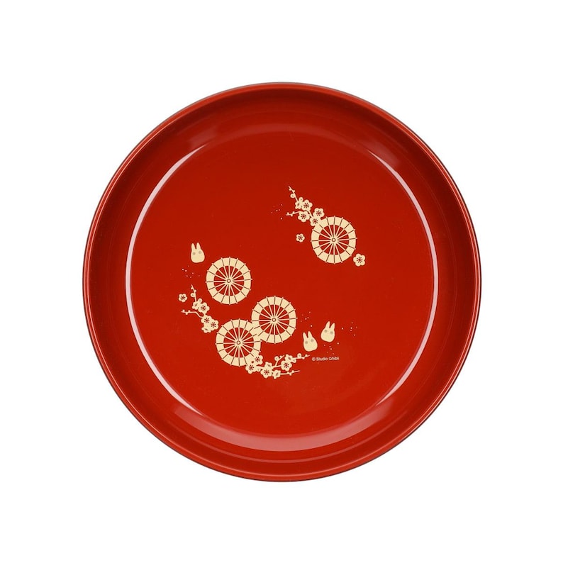 May include: A round, red serving tray with a glossy finish. The tray features a decorative pattern of stylized wheels, flowers, and small rabbit figures in a cream color. The design is arranged across the surface of the tray.
