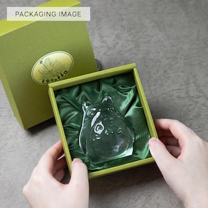 May include: A clear glass figurine of a cartoon character inside a green box with a green satin lining. The box is olive green with a gold emblem and text. The words "PACKAGING IMAGE" are in a white box in the top left corner.
