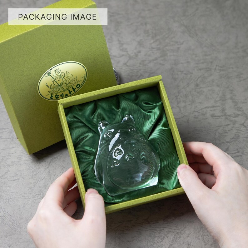 May include: A clear glass figurine of a cartoon character inside a green box with a green satin lining. The box is olive green with a gold emblem and text. The words "PACKAGING IMAGE" are in a white box in the top left corner.