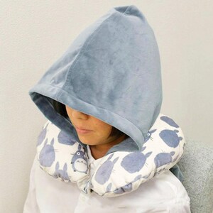 May include: A light blue hooded travel pillow with a Totoro design. The hood is a soft, plush material. The pillow features a pattern of blue Totoro characters on a white background.