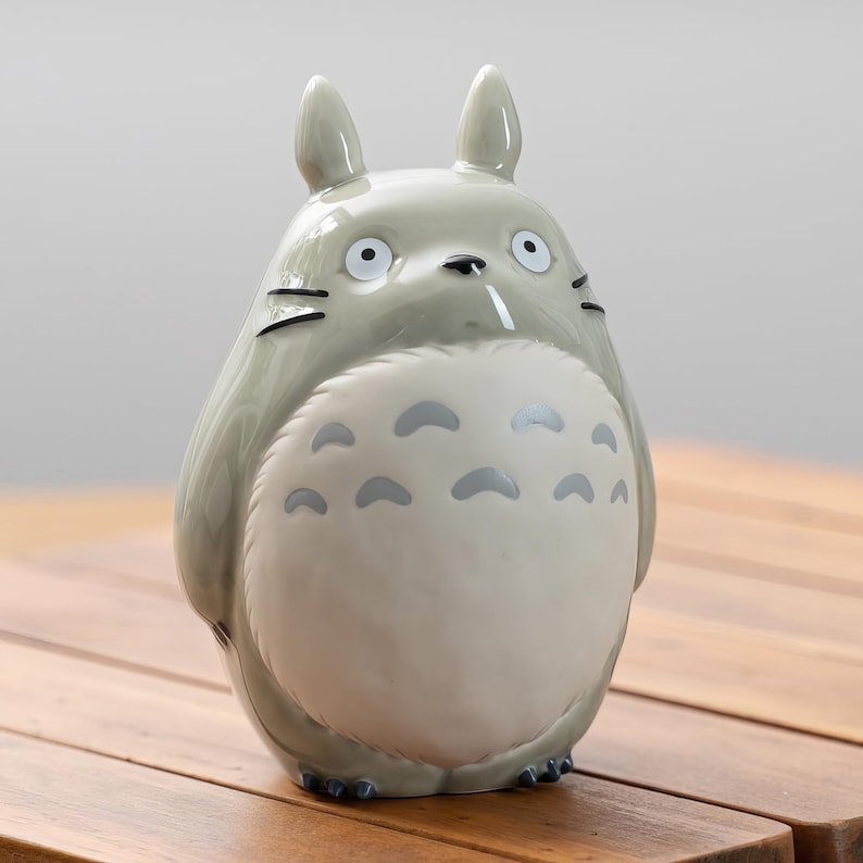 Puede incluir: Figura de cer&aacute;mica gris de un personaje de dibujos animados con ojos grandes, orejas puntiagudas y vientre blanco con marcas grises. La figura est&aacute; sobre una superficie de madera.