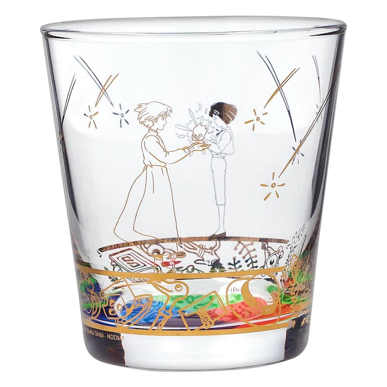 May include: Clear glass tumbler featuring a gold illustration of two figures and fireworks. The bottom of the glass has a colorful, patterned border. The glass is a collectible item.