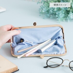 May include: A gold-toned clutch purse with a light blue satin lining. The purse is open and has several makeup brushes and a lipstick inside.