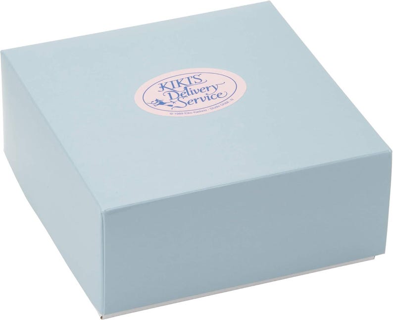 May include: A light blue square box with a matching lid. An oval sticker on the lid reads "KIKI'S Delivery Service" in pink and white text. The box is likely for packaging or gifting.