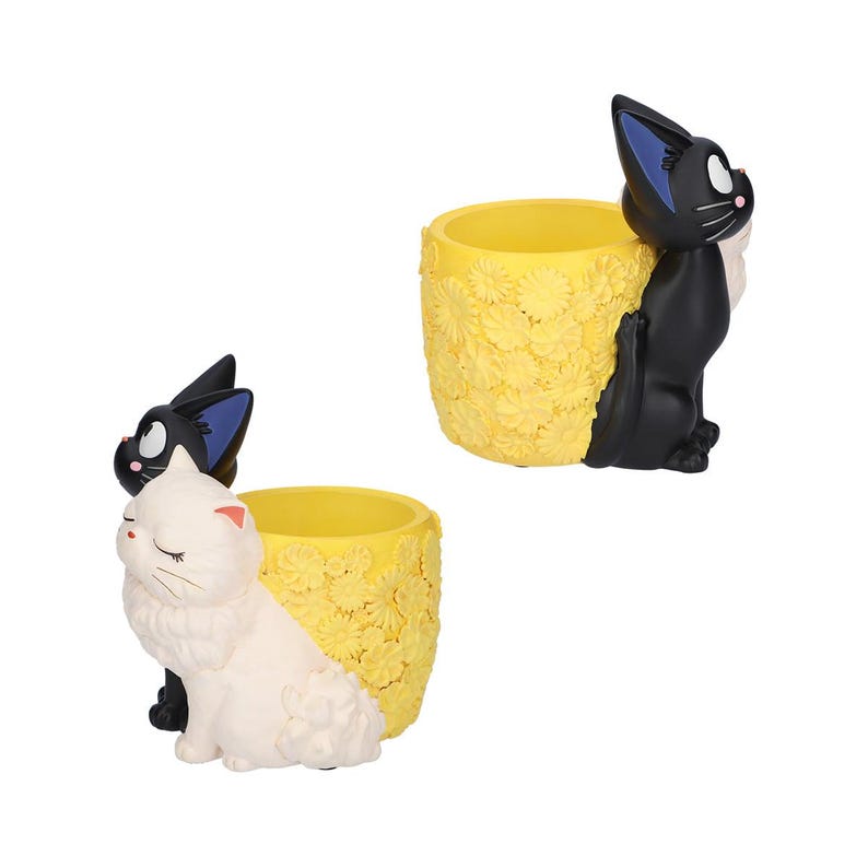 Puede incluir: Dos macetas cil&iacute;ndricas con exterior amarillo y un patr&oacute;n floral texturizado. Una maceta presenta un gato negro con orejas bordeadas en azul, mientras que la otra tiene un gato blanco con ojos cerrados y orejas con puntas rosadas.