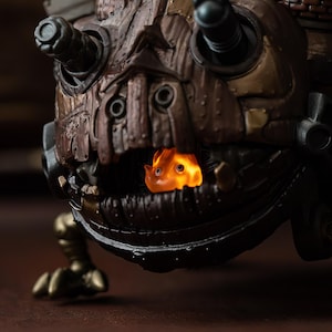 May include: Close-up of a detailed, steampunk-style sculpture with a brown and bronze color scheme. The sculpture features mechanical details and a glowing orange creature inside its mouth, creating a striking visual contrast.