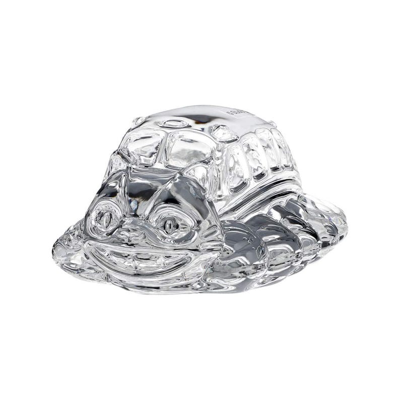 May include: A clear glass turtle figurine with a smiling face and textured shell. The figurine has a wide base and is designed with detailed features, creating a whimsical and decorative piece.