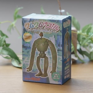 Peut inclure: Bo&icirc;te de puzzle 3D avec un personnage de robot vert. La bo&icirc;te contient du texte japonais et les mots anglais &laquo;&nbsp;3D JIGSAW PUZZLE&nbsp;&raquo;. Le tout est pos&eacute; sur une surface en bois.