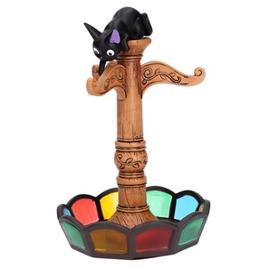 May include: A decorative stand featuring a black cat figurine with purple ear accents perched atop a brown, ornate column. The column has a stained glass base with red, yellow, green, and blue panels. The stand has a whimsical, artistic design.