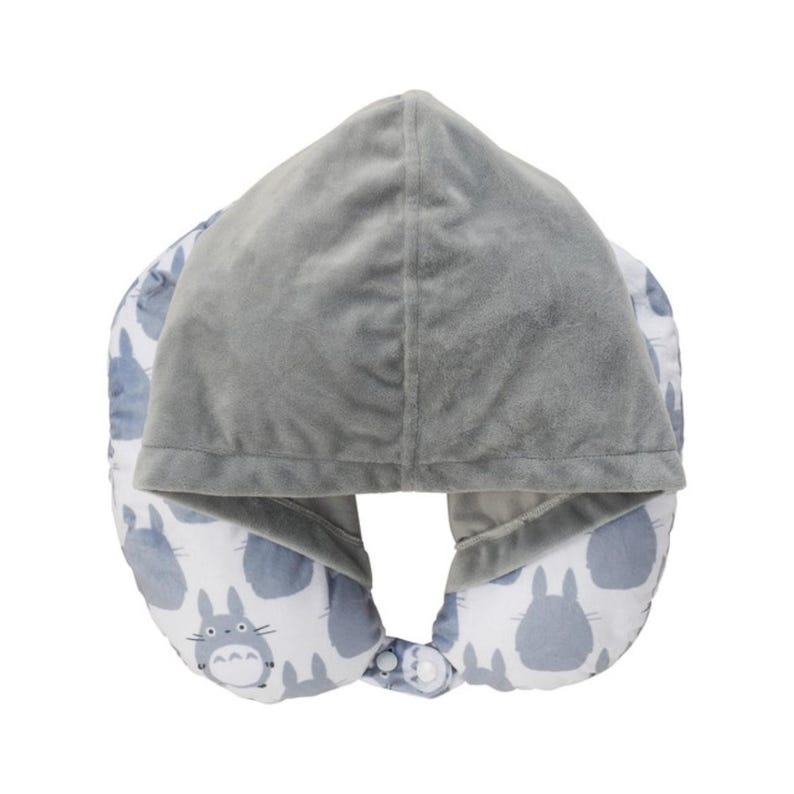 May include: A gray travel pillow with a hood. The hood and the top of the pillow are a solid gray color. The bottom of the pillow is white with a pattern of blue cartoon characters. The pillow has a snap closure.