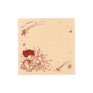May include: A square wooden rubber stamp featuring a dark red engraved illustration of a person with short hair holding a glowing, star-like burst of light. The design includes scattered stars and shooting star trails across the light wood surface.