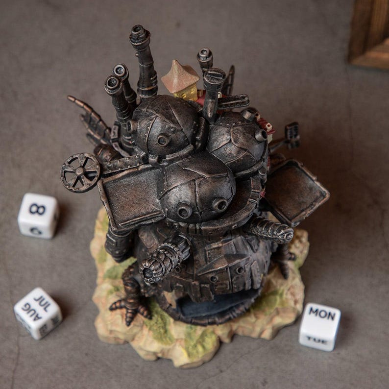 May include: A detailed, steampunk-style sculpture with a metallic finish, featuring multiple mechanical components, turrets, and a small house. The sculpture sits on a textured base with three dice nearby, each displaying different numbers and months.