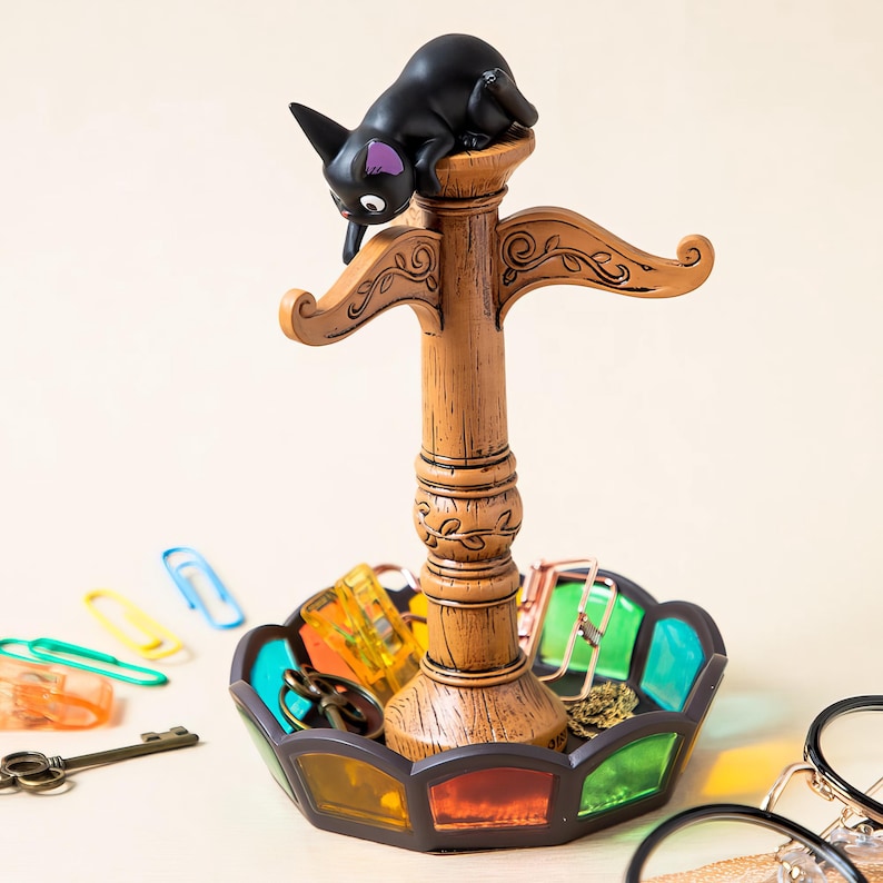 May include: A decorative black cat figurine atop a wooden key and accessory holder. The holder features a stained glass-style tray with various items, including keys and paper clips. The cat has purple accents on its ears.