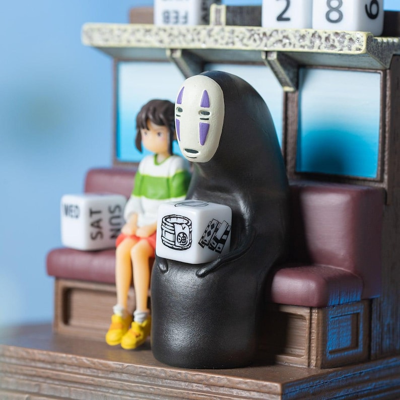 May include: A detailed figurine featuring characters from the animated film Spirited Away. The black figure holds a white cube with illustrations. A girl in a green and white shirt sits on a bench. The calendar shows the date February 28.