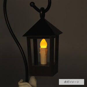 May include: Black metal lantern with a faux candle inside, emitting a warm yellow glow. The lantern has a peaked roof and a handle for hanging. The candle is a cream color with a melted wax effect.