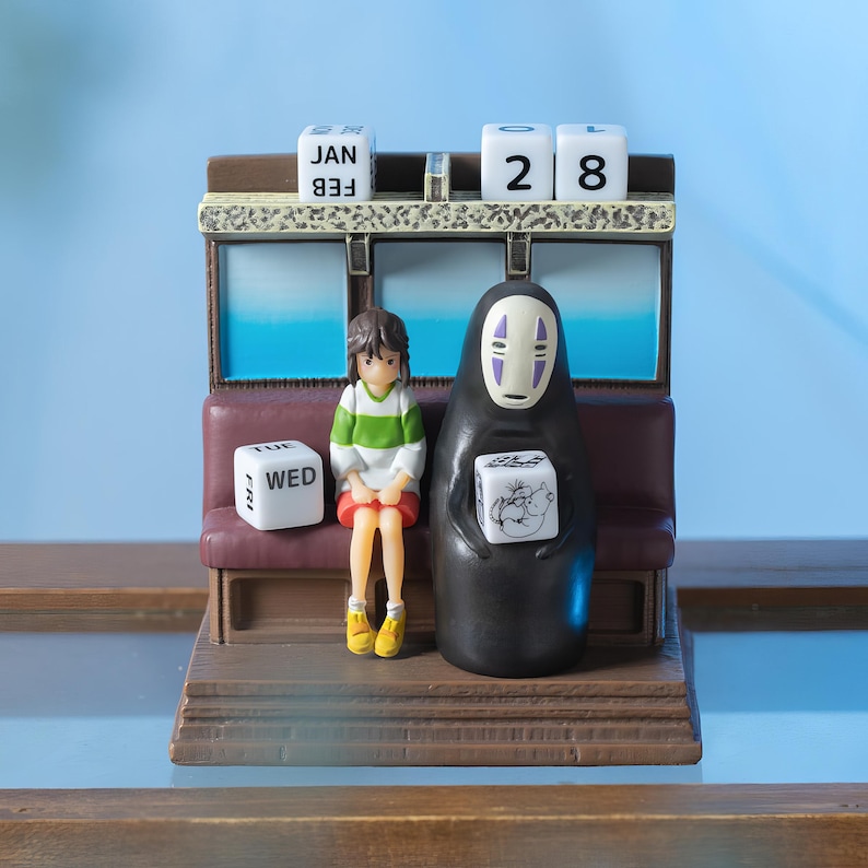 May include: A decorative figurine featuring characters from a popular animated film. The figurine includes a seated girl in a green and white striped shirt and a tall, black figure. The figurine has a calendar with the date January 28.