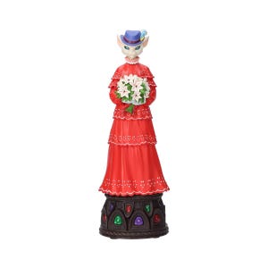 Puede incluir: Figura decorativa de un personaje felino con un vestido rojo y un sombrero azul, sosteniendo flores blancas. La figura tiene una base detallada con acentos coloridos.