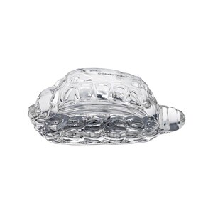 May include: A clear glass turtle figurine with textured shell details. The figurine has a rounded body and a small head and tail. The text "Studio Ghibli" is printed on the top of the figurine.