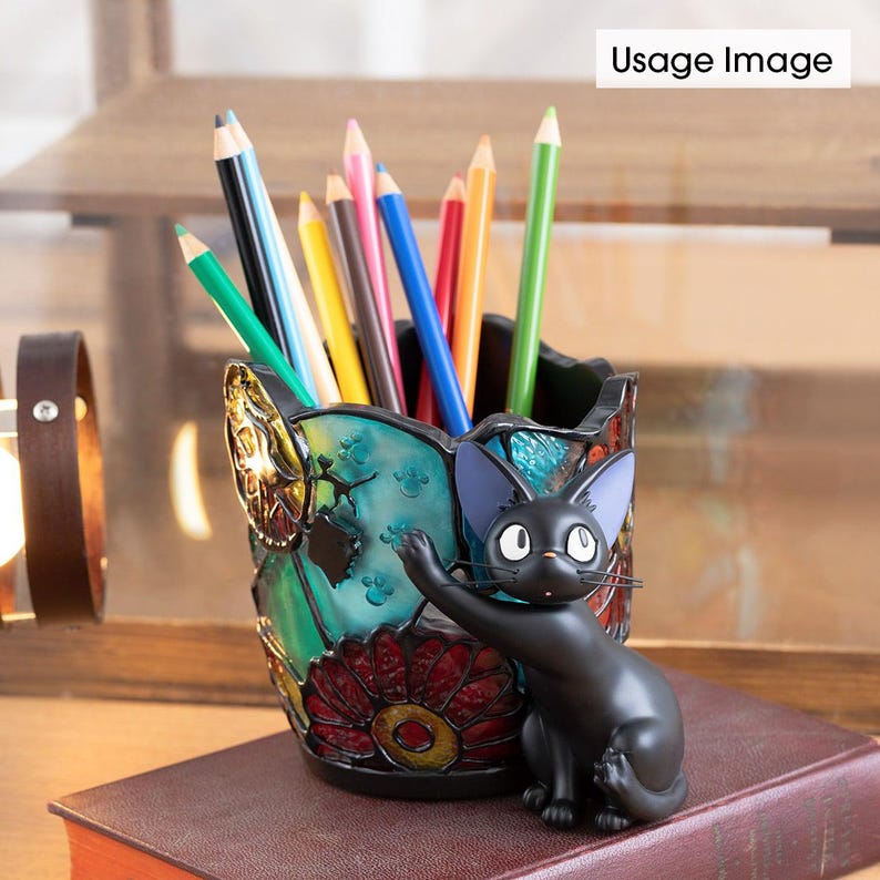 K&ouml;nnte beinhalten: Ein Bleistifthalter aus Buntglas mit einer schwarzen Katzenfigur. Der Halter hat ein florales Design mit roten, gelben und blauen Akzenten. Die Katze h&auml;lt eine Pfote hoch und hat ein schwarz-wei&szlig;es Gesicht.