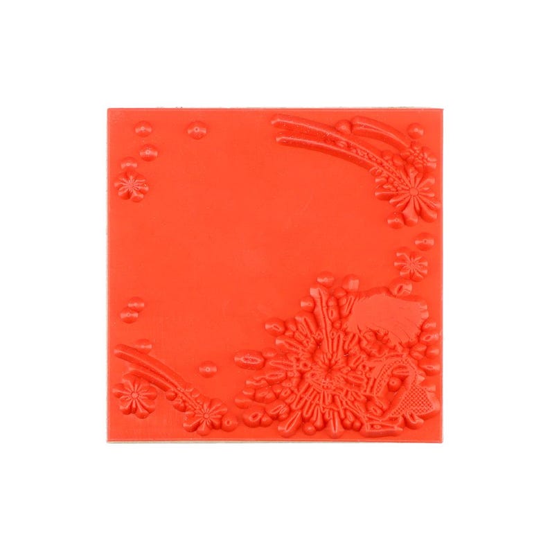 May include: A square, bright orange rubber stamp sheet featuring a raised, embossed design of floral elements and small circular dots arranged in the corners, creating a decorative pattern for crafting and stamping applications.