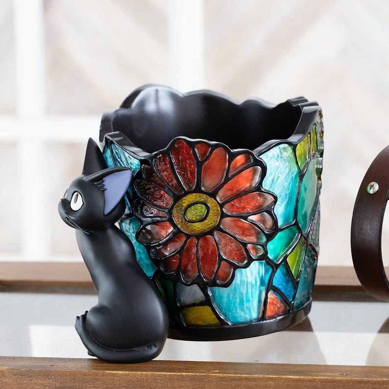 K&ouml;nnte beinhalten: Eine schwarze Katzenfigur mit einem Bleistiftst&auml;nder im Stil von Buntglas mit einem roten Blumendesign. Der Bleistiftst&auml;nder hat ein blaues, gr&uuml;nes und gelbes Mosaikmuster.