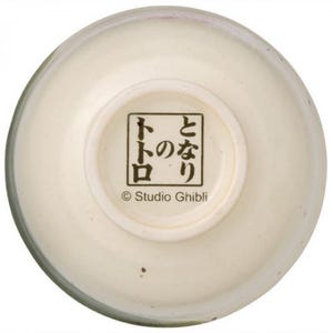 May include: Cream-colored ceramic bowl with a rounded shape. The bottom of the bowl features Japanese text within a square frame, along with the text "&copy; Studio Ghibli". The bowl has a glossy finish.