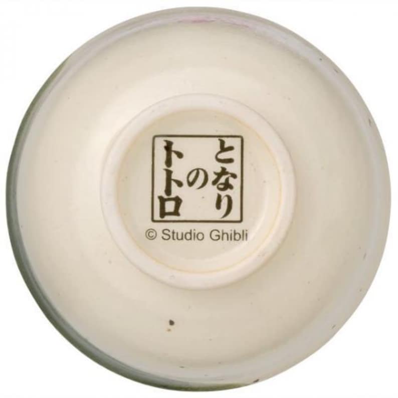 May include: Cream-colored ceramic bowl with a rounded shape. The bottom of the bowl features Japanese text within a square frame, along with the text "&copy; Studio Ghibli". The bowl has a glossy finish.