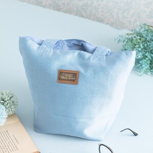 May include: A light blue canvas tote bag with a brown leather patch that says "Kiki's Delivery Service".