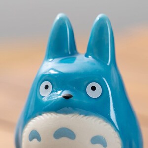 May include: A blue ceramic figurine of a cartoon character with large eyes, pointed ears, and a white belly with three dark blue markings. The figurine has a glossy finish and a small black nose.