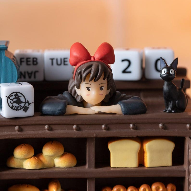 Pode incluir: Figura detalhada com uma jovem com um la&ccedil;o vermelho, um gato preto e um calend&aacute;rio exibindo "FEB TUE 2". A cena inclui p&atilde;es em miniatura e uma prateleira de padaria, evocando um tema caprichoso e animado.