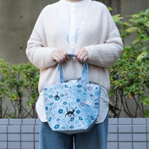 May include: A light blue tote bag with a floral pattern and embroidered black cats. The bag has two handles and is made of a soft fabric.