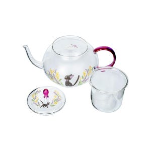 Puede incluir: Una tetera de cristal transparente con asa morada y tapa a juego. La tetera presenta un gr&aacute;fico de un gato negro rodeado de ramitas florales amarillas y moradas. Un infusor de t&eacute; de cristal transparente se encuentra junto a la tetera.