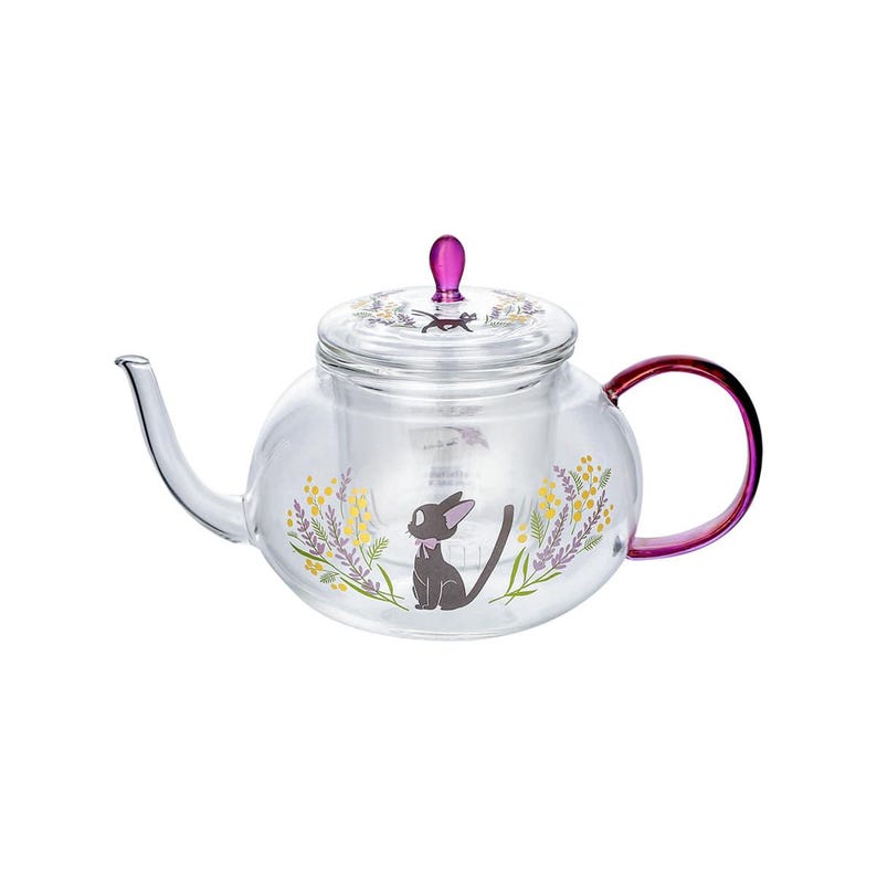 Puede incluir: Una tetera de cristal transparente con una ilustraci&oacute;n de un gato negro con un lazo rosa, rodeado de motivos florales amarillos y morados. La tetera tiene un pomo de tapa morado y un asa morada, con un gr&aacute;fico de gato a juego en la tapa.
