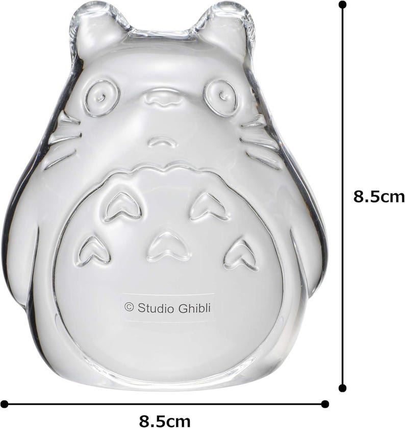 May include: A clear glass figurine in the shape of a cartoon character, 8.5 cm tall and 8.5 cm wide. The character has large eyes, a round belly, and pointed ears. The Studio Ghibli logo is printed on the bottom.