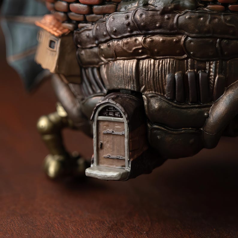 May include: Close-up of a detailed, steampunk-style sculpture. The sculpture features a miniature house with a small door, brickwork, and metallic panels in shades of brown, bronze, and copper. The design suggests a fantastical, mechanical theme.