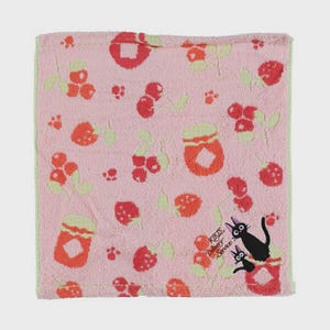 May include: A pink hand towel with a pattern of red berries, jam jars, and green leaves. The towel has a light green border and features a black cat illustration with the text "KIKIS Delivery Service".