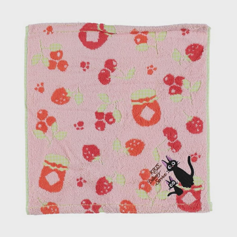 May include: A pink hand towel with a pattern of red berries, jam jars, and green leaves. The towel has a light green border and features a black cat illustration with the text "KIKIS Delivery Service".