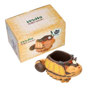 May include: A tan and yellow pen stand shaped like a cat-like creature with a brown tail and accents. The pen stand is next to a box with Japanese text and a cartoon image of the pen stand. The box has a sticker that says "PINSTAND".