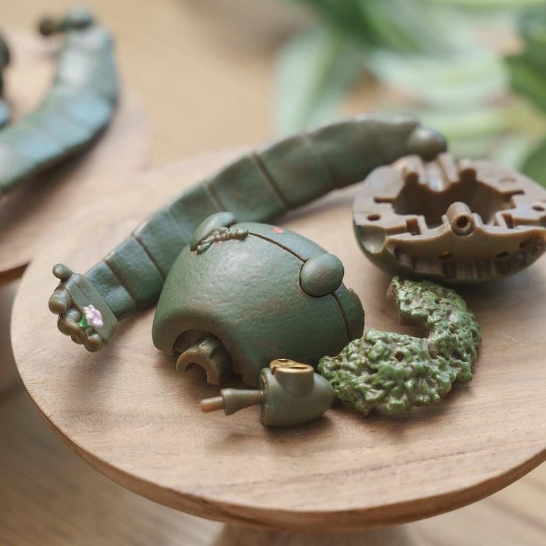 Peut inclure: Divers &eacute;l&eacute;ments de jouets vert olive, dont une t&ecirc;te, un bras et d'autres composants, sont dispos&eacute;s sur une surface en bois. Le bras pr&eacute;sente un petit d&eacute;tail floral. Les pi&egrave;ces semblent provenir d'un jouet plus grand.