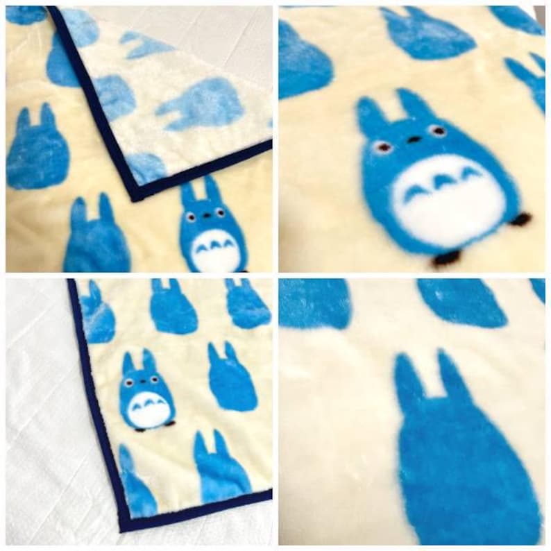 May include: A plush blanket featuring a repeating pattern of blue cartoon characters on a cream background. The blanket has a navy blue border. The characters have a white belly and a blue outline.
