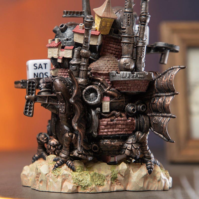 May include: A detailed, steampunk-style sculpture of a fantastical castle with wings, chimneys, and miniature buildings. The sculpture is primarily bronze and brown with red brick accents. A small sign reads "SAT SUN".
