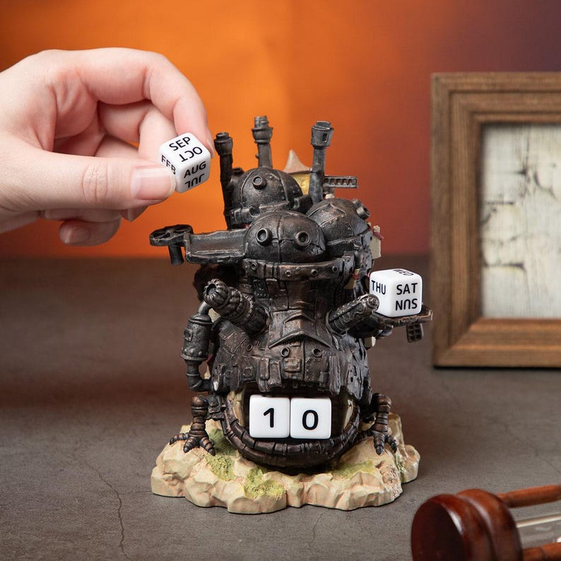 May include: A detailed, dark brown perpetual calendar shaped like a mechanical structure. The calendar displays the date as "10" and includes dice for the month and day of the week. The base is a light brown color, and a hand is holding a month die.