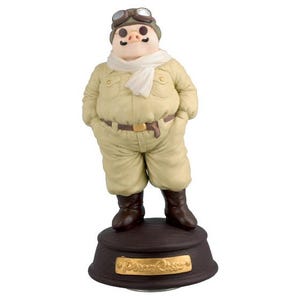 May include: A figurine of a pig in a pilot's outfit, featuring a tan jumpsuit, goggles, and a white scarf. The pig stands on a brown base with gold lettering that reads "Porco Rosso". The figurine has brown boots and a brown belt.